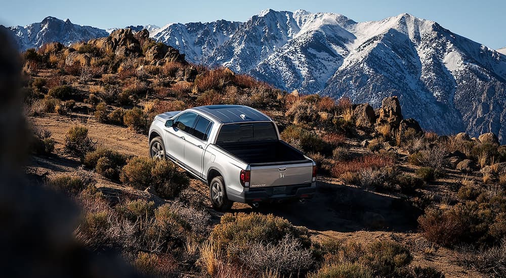 A silver 2022 Honda Ridgeline RTL-E is shown from a rear angle off-roading on a mountain path.