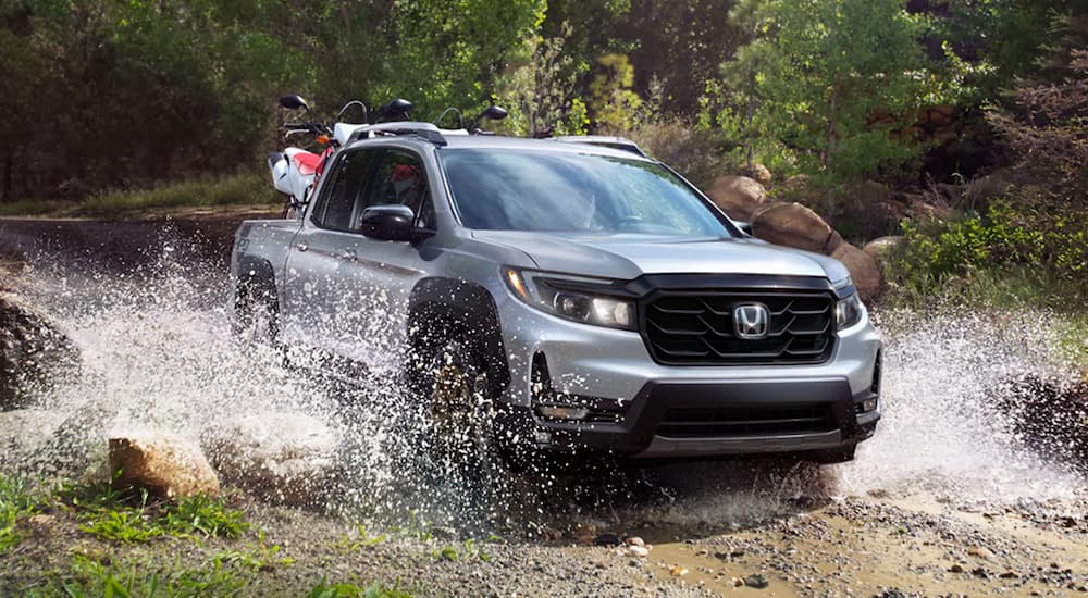 A silver 2022 Honda Ridgeline Sport is shown off-roading through a body of water.