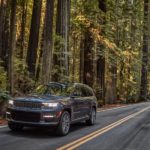 A grey 2022 Jeep Grand Cherokee L Summit Reserve is shown driving down a road in a forest.
