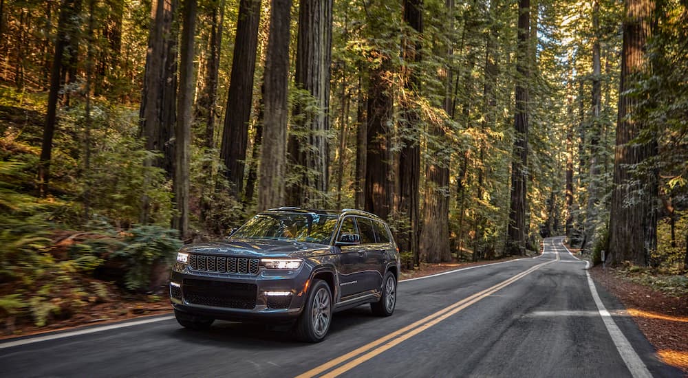 A grey 2022 Jeep Grand Cherokee L Summit Reserve is shown driving down a road in a forest.