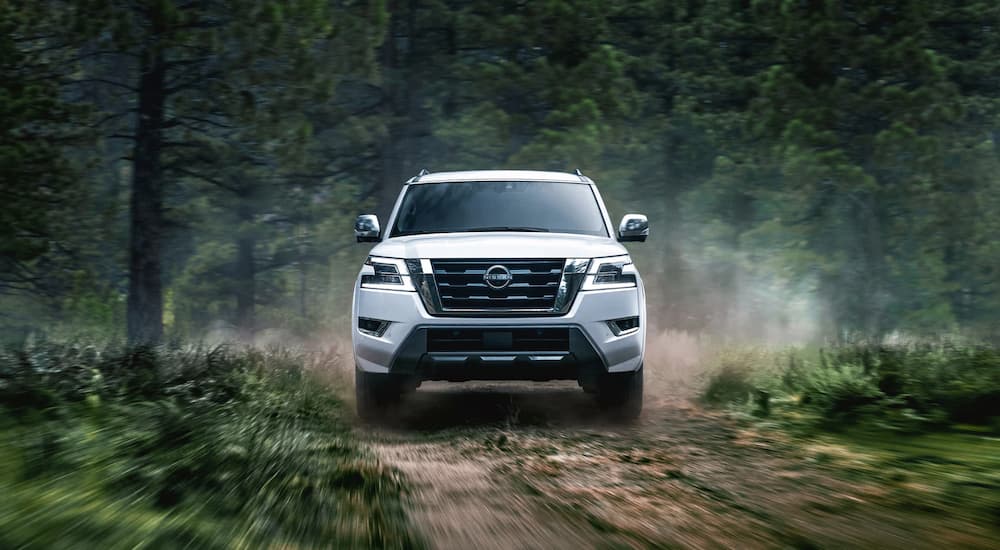 A white 2022 Nissan Armada is shown from the front driving on a forest road.