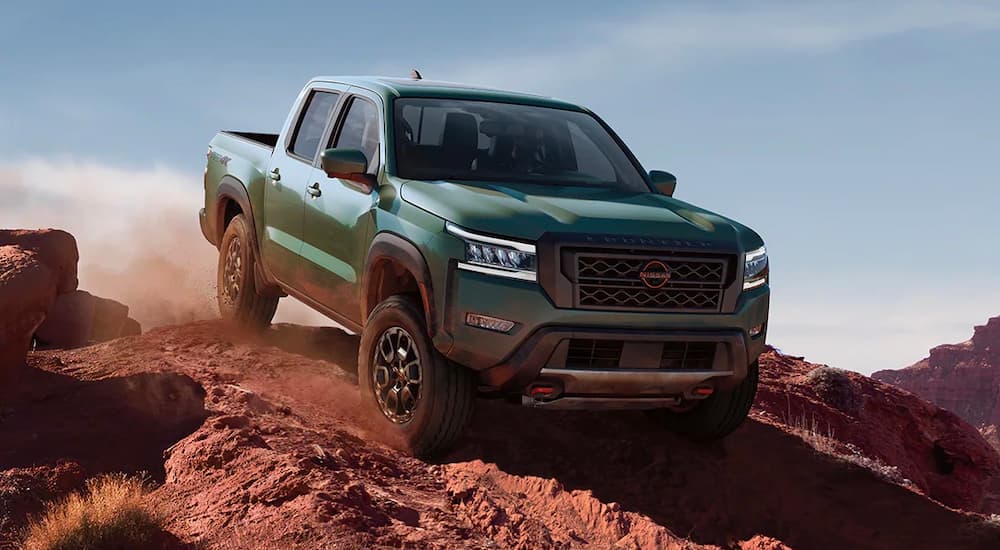 A green 2022 Nissan Frontier PRO-4X is shown off-roading on a dusty path.
