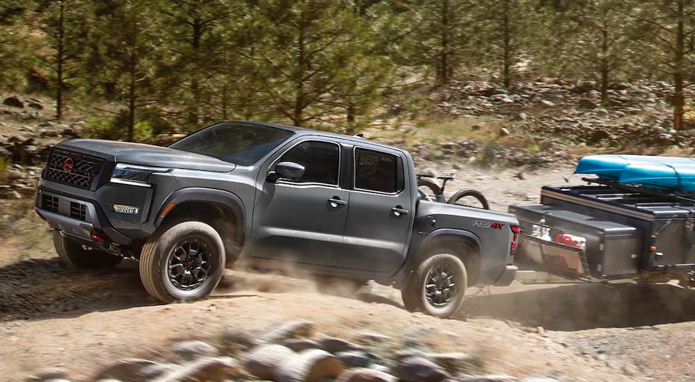 A grey 2022 Nissan Frontier PRO-4X is shown towing a small trailer on a dirt road.