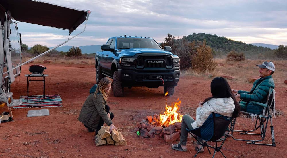 A blue Ram 2500 is shown parked next a family enjoying a campfire.