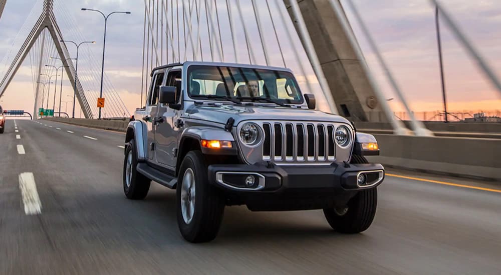 A silver 2021 Jeep Wrangler is shown driving on a bridge.