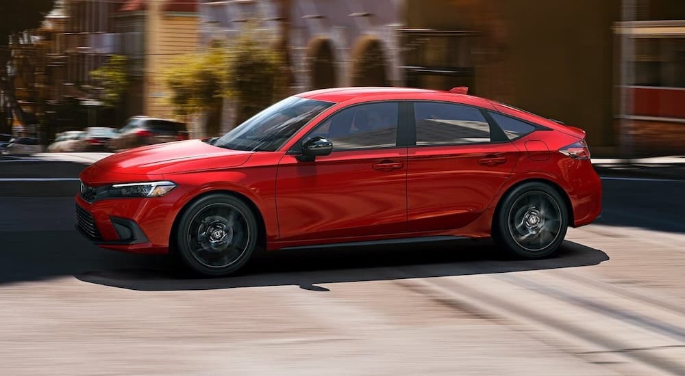 A red 2022 Honda Civic Hatchback Sport is shown driving through a city.