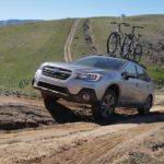 A silver 2018 Subaru Outback is shown driving up a steep dirt road.