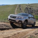 A silver 2018 Subaru Outback is shown driving up a steep dirt road.