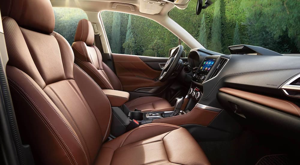 The brown and black interior of a 2021 Subaru Forester shows the front seats and steering wheel.