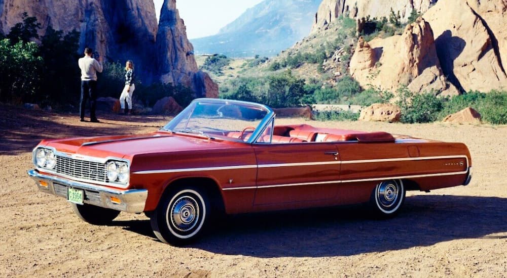 A red 1964 Chevy Impala Convertible is shown parked in a rocky mountain area.