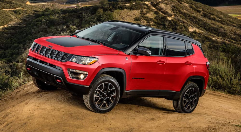 A red 2022 Jeep Compass Trailhawk is shown driving on a dirt road.