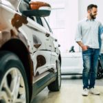 A couple is shown at a pre-owned car dealer next to a red SUV.