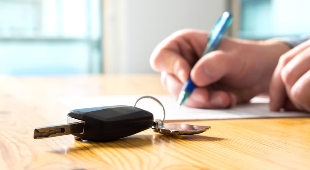 A person is shown filling out paperwork at a pre-owned car dealer.