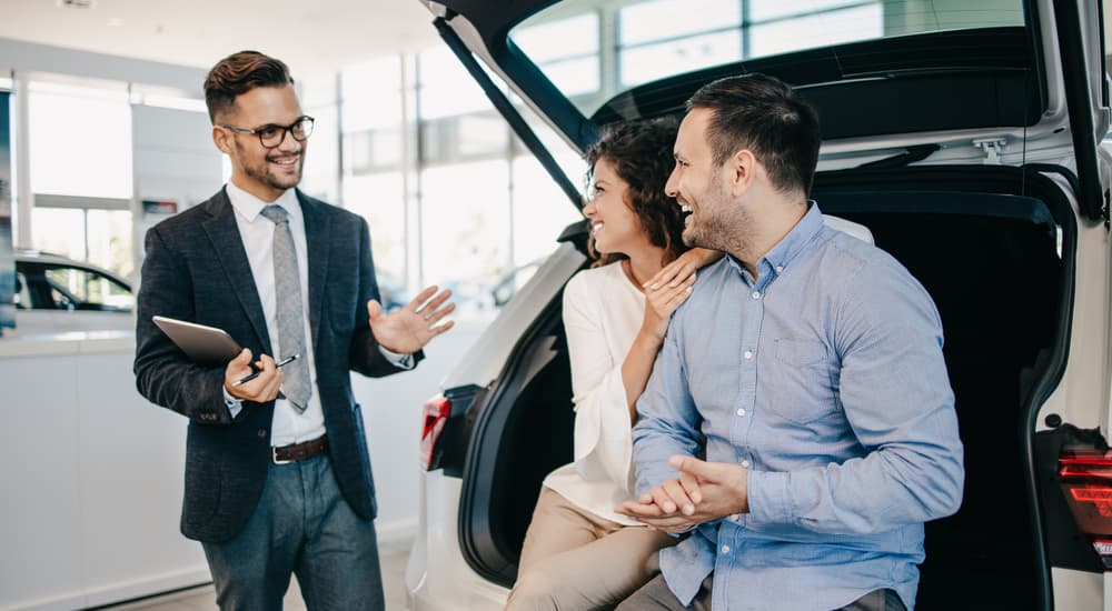 A car salesman is shown speaking to a couple who asked how to 'sell my car.'