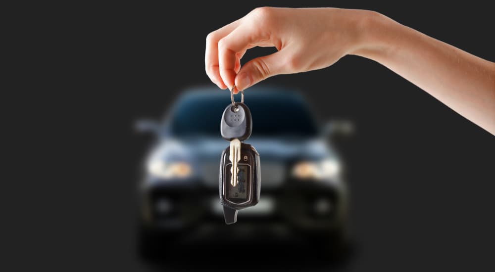 A person is shown holding a set of car keys in front a car on a dark background.