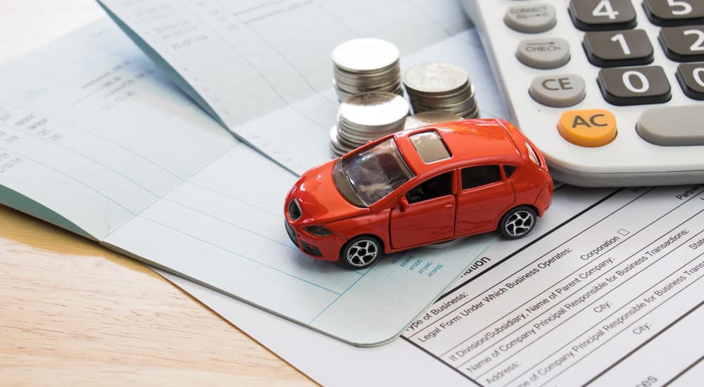 An orange toy car is shown on top of paperwork next to a calculator.