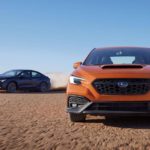 An orange and a black 2022 Subaru WRX are shown driving in the open desert.