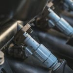 A close up shows blue fuel injectors on a vehicles fuel rail.