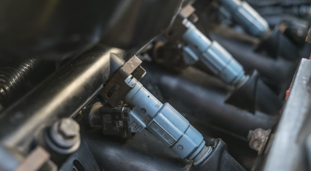 A close up shows blue fuel injectors on a vehicles fuel rail.