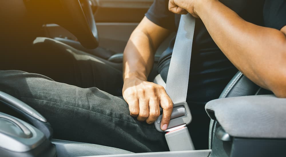 A close up shows a person buckling a seatbelt before they visit a used car dealership.