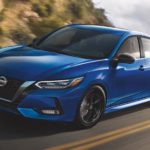 A blue 2021 Nissan Sentra is shown driving down a road during a 2021 Nissan Sentra vs 2021 Toyota Corolla comparison.