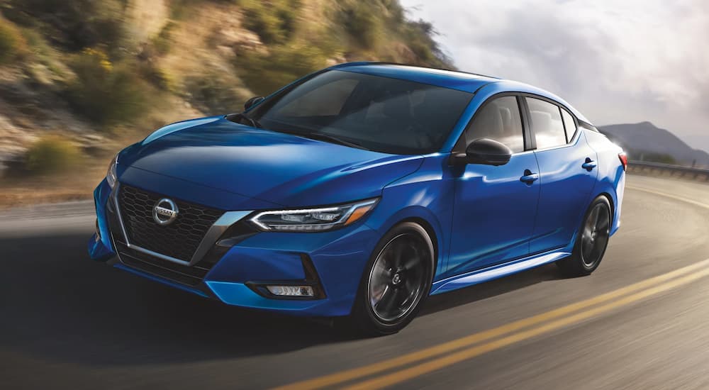 A blue 2021 Nissan Sentra is shown driving down a road during a 2021 Nissan Sentra vs 2021 Toyota Corolla comparison.