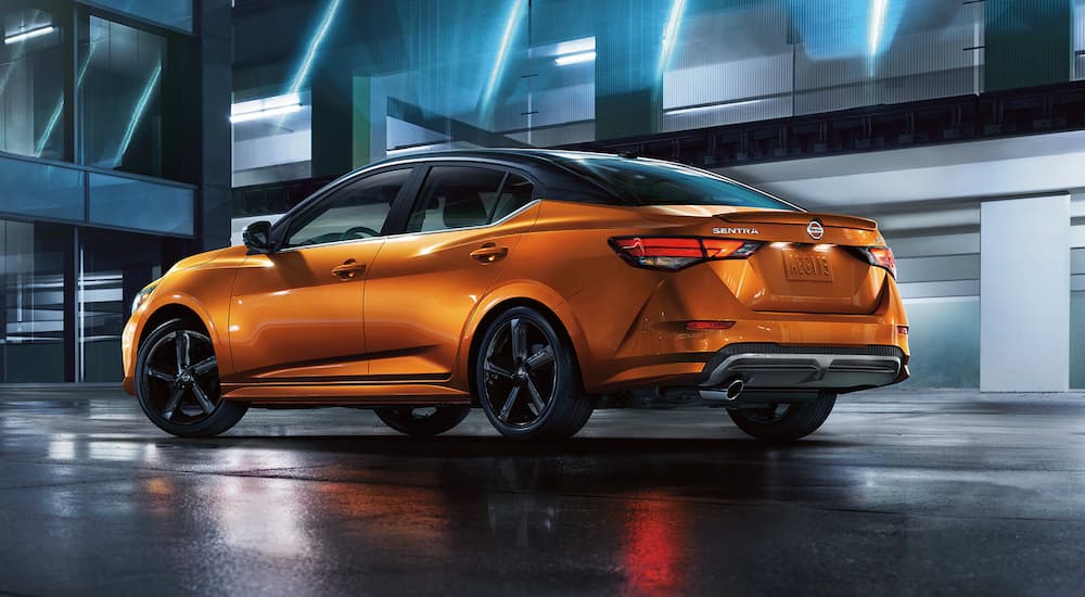 An orange 2021 Nissan Sentra is shown from a rear angle driving down a city street.