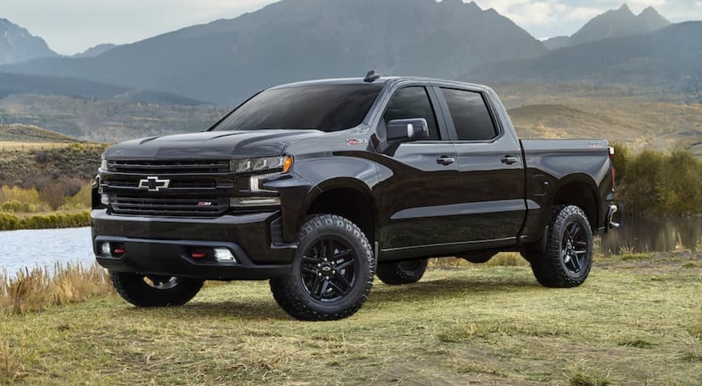 A black 2022 Chevy Silverado 1500 is shown from the side parked in a grass field in front of a stream.