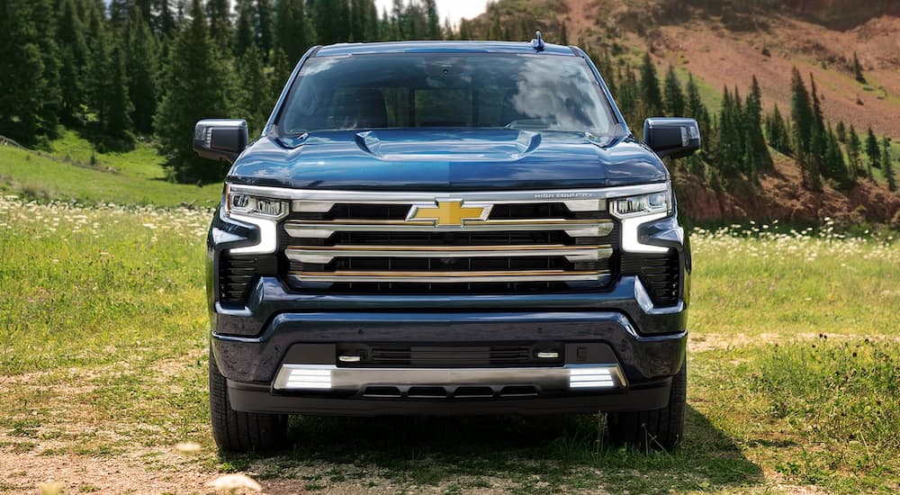 A blue 2022 Chevy Silverado 1500 High Country is shown from the front parked in a grassy field.