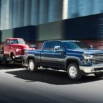 A blue 2022 Chevy Silverado 2500 HD is shown towing a red truck.