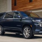 A blue 2022 Chevy Suburban is shown from the side parked in front of a modern house.