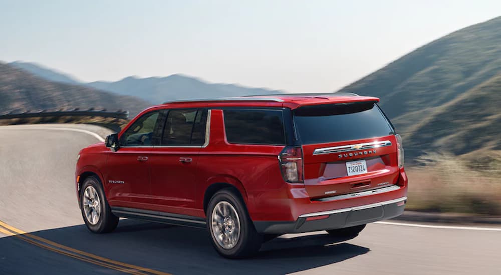 A red 2022 Chevy Suburban is shown from the side driving on an open road past mountains.