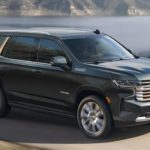 A black 2022 Chevy Tahoe High Country is shown from the side driving on an open road past a lake.