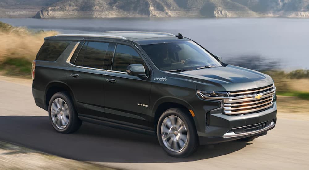 A black 2022 Chevy Tahoe High Country is shown from the side driving on an open road past a lake.