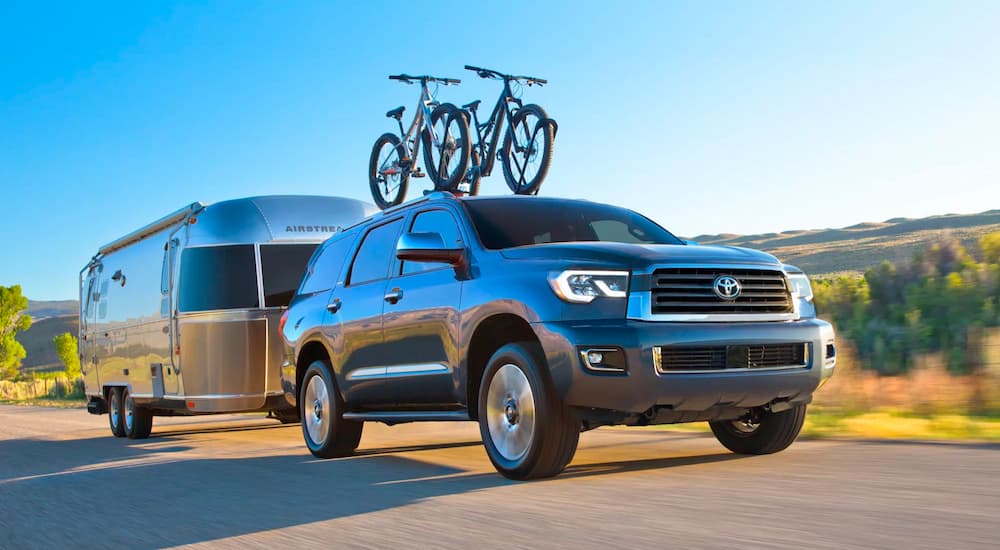 A silver 2022 Toyota Sequoia is shown towing a trailer down a desert highway.