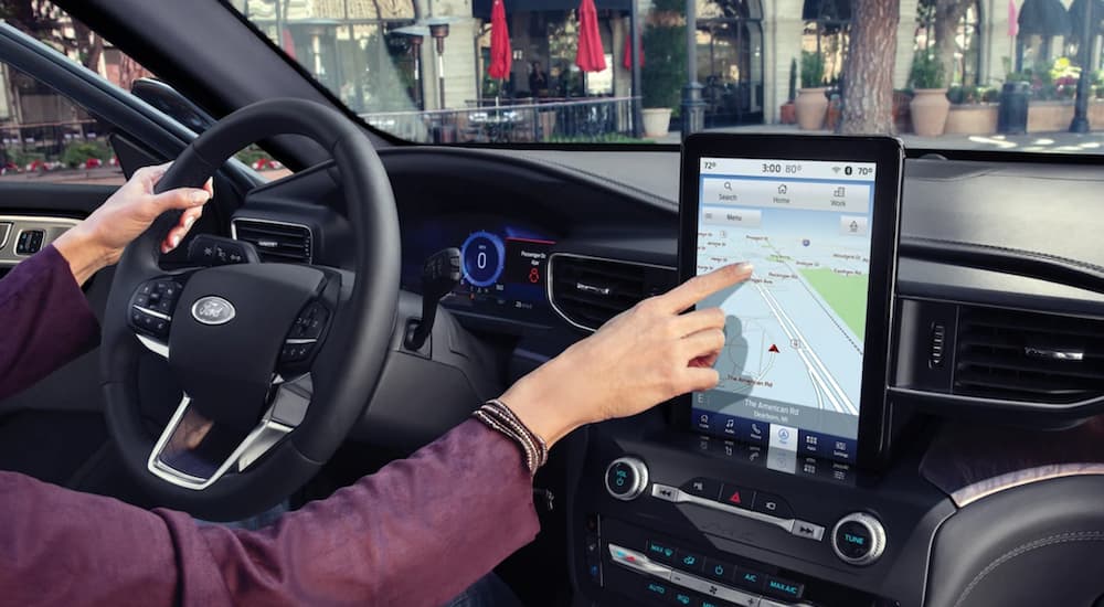 The black interior of a 2022 Ford Explorer ST shows a person touching the infotainment screen.