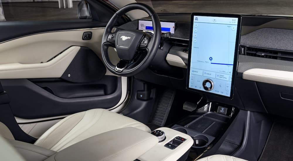 The white and black interior of a 2022 Ford Mustang Mach-E Ice White Edition shows the steering wheel and infotainment screen.
