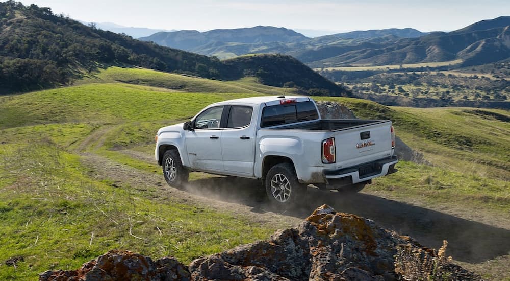 A white 2022 GMC Canyon is shown from a rear angle driving through a grassy field.