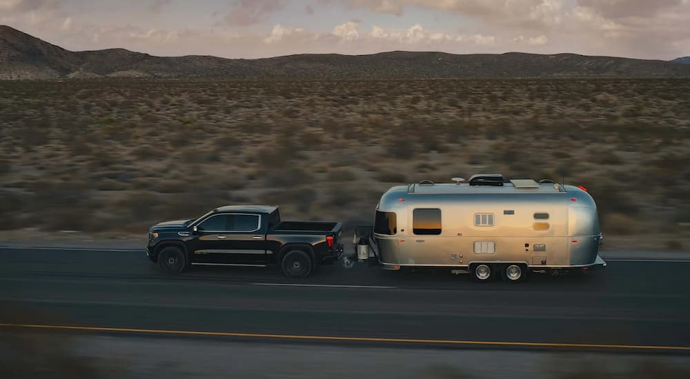 A black 2022 GMC Sierra 1500 is shown from the side towing a trailer on an open road.