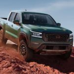 A green 2022 Nissan Frontier PRO-4X is shown off-roading on a dusty desert path.