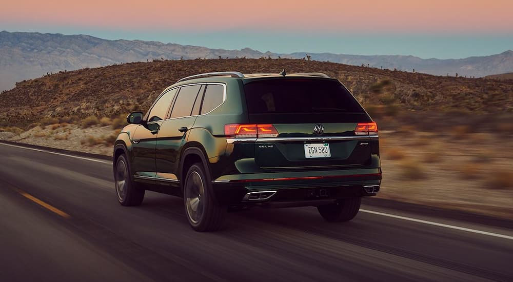 A green 2022 Volkswagen Atlas SEL is shown from a rear angle driving on a highway in the desert.