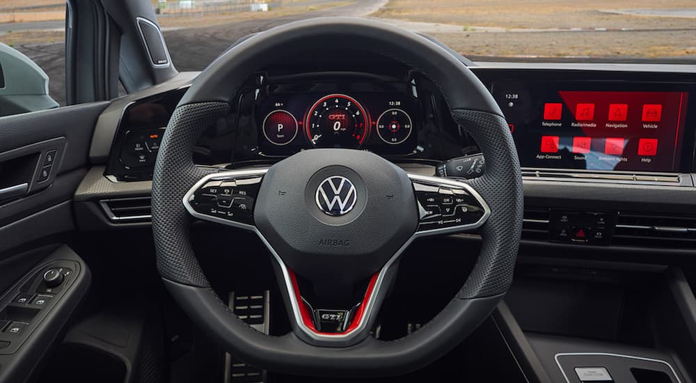 The black interior of a 2022 Volkswagen Golf GTI shows the steering wheel and infotainment screen.