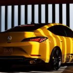 A yellow 2023 Acura Integra is shown from the rear parked in a modern garage.