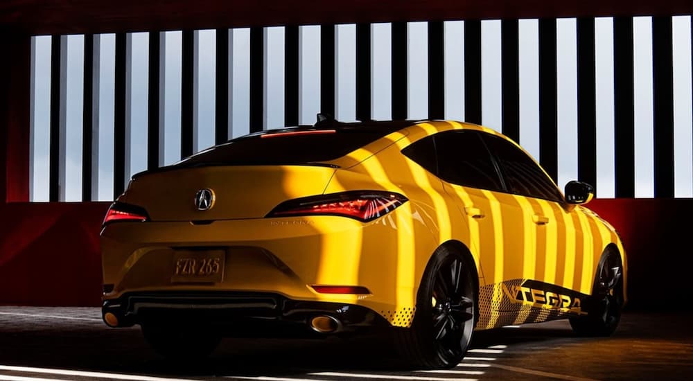 A yellow 2023 Acura Integra is shown from the rear parked in a modern garage.