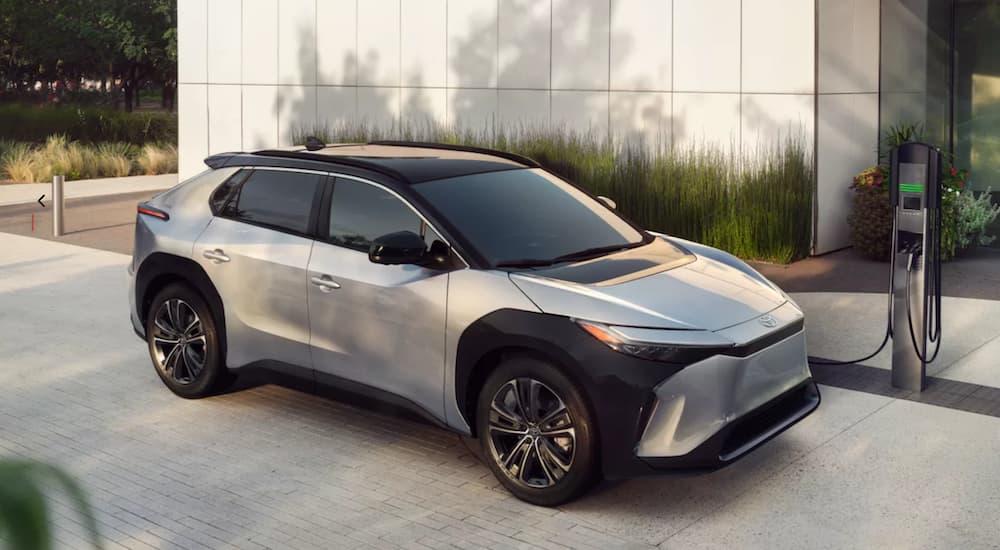 A silver 2023 Toyota bZ4x Limited is shown from the side parked in front of a modern house while charging.