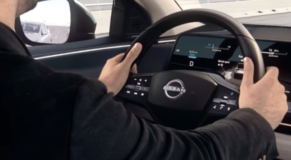 The black interior of a 2023 Nissan ARIYA shows a person gripping the steering wheel.