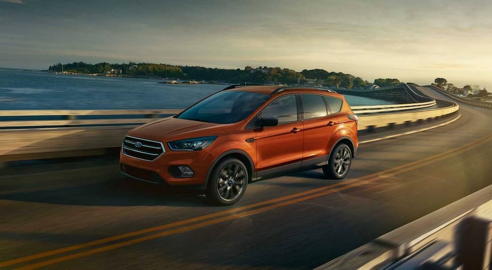 An orange 2019 Ford Escape is shown from the side driving on an open road past a lake after leaving a Certified Pre-Owned Ford Escape dealer.
