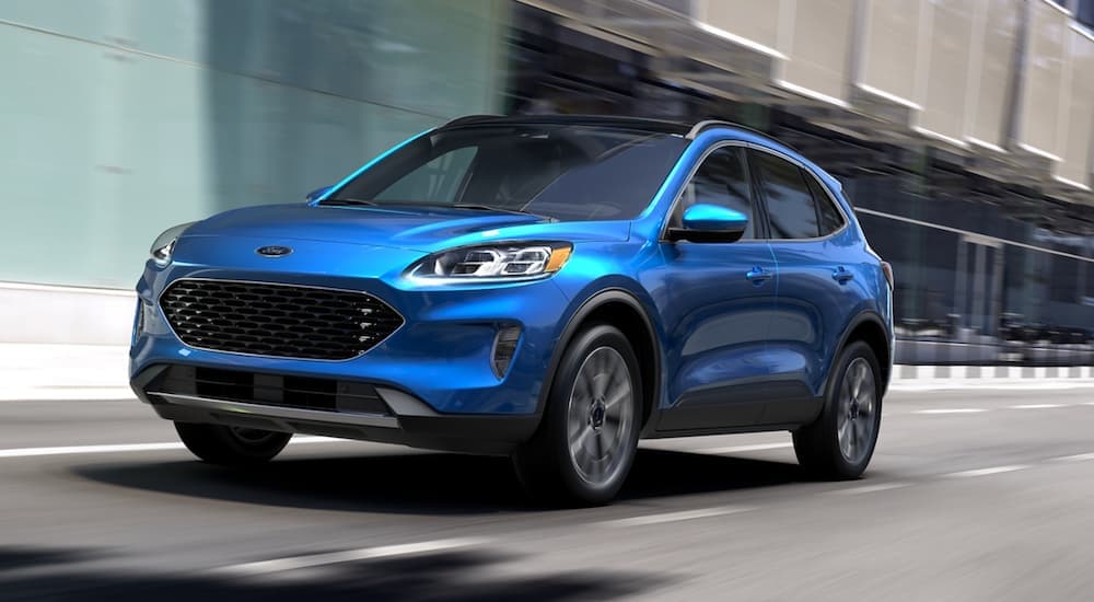 A blue 2020 Ford Escape is shown from the front driving through a city.
