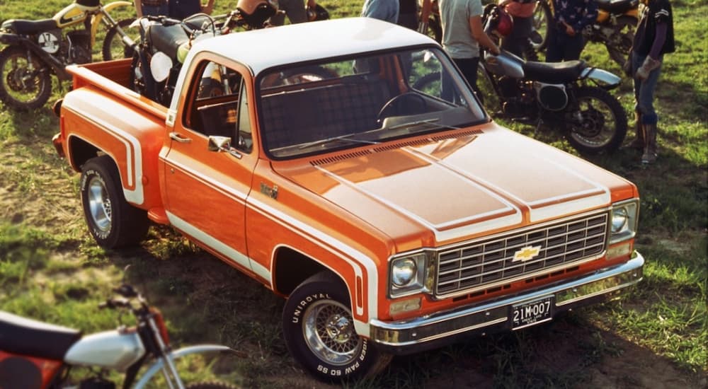 An orange 1976 Chevy C10 Stepside is shown parked in a grassy field.