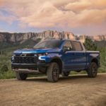 A blue 2022 Chevy Silverado 1500 ZR2 is shown from the side parked on a dirt road in the mountains at sunset.